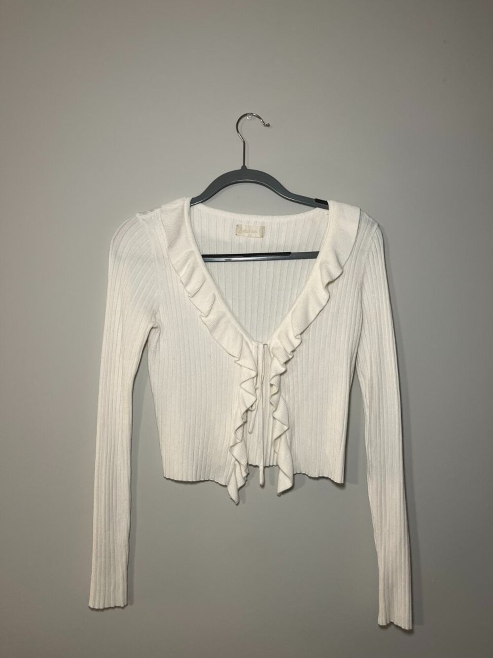 white ribbed cardigan featuring a ruffled V-neckline and tie-front closure.